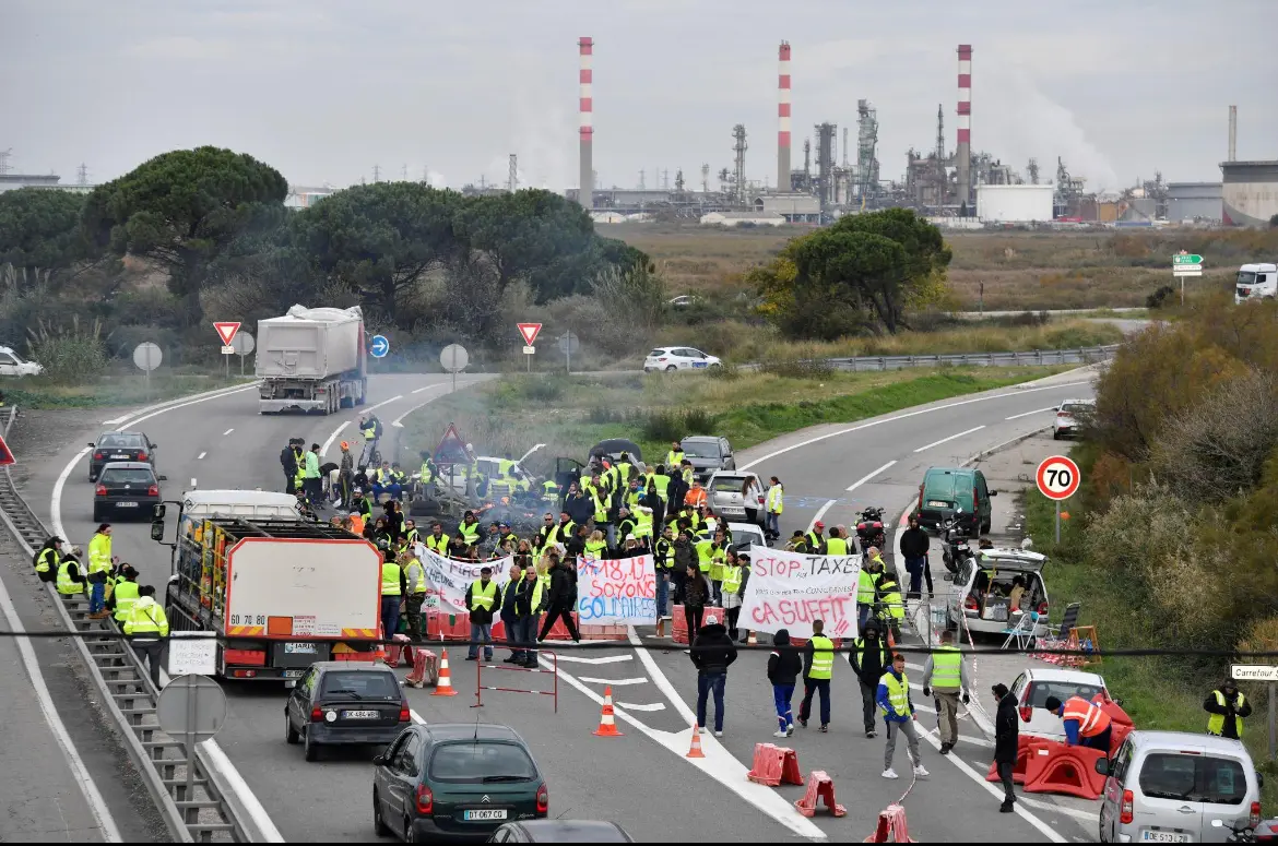 Des manifestants en gilets jaunes bloquant une route près d’un site industriel, photographie d’illustration