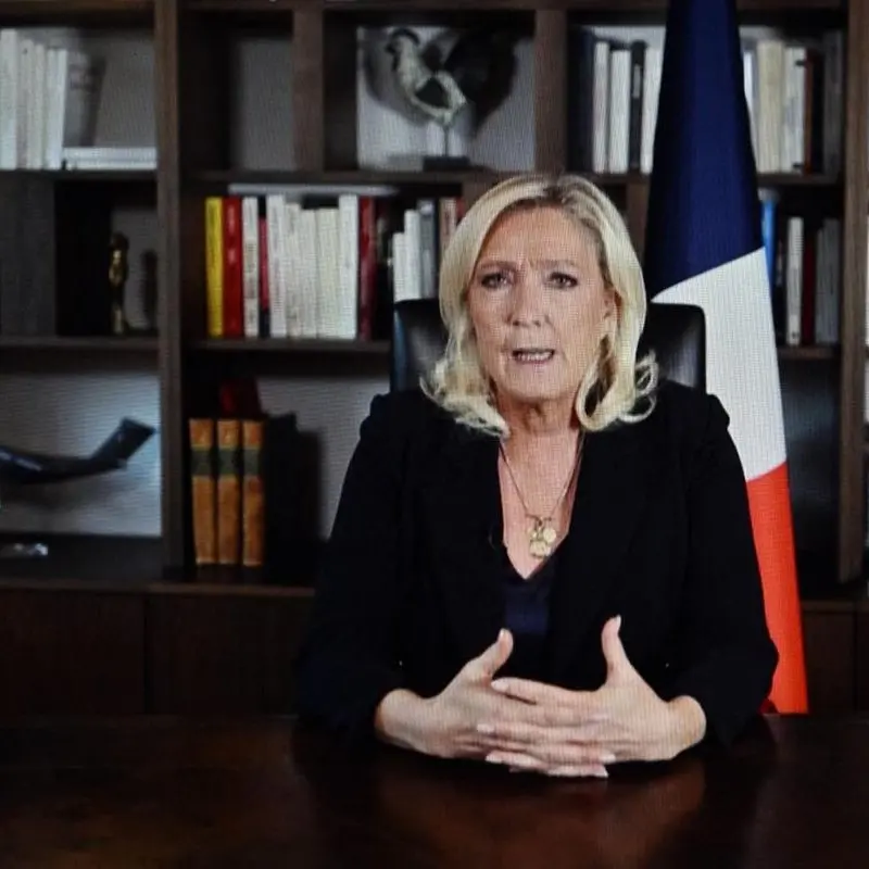 Marine Le Pen assise à un bureau devant un drapeau français, photographie d’illustration