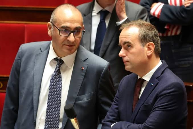 Sébastien Lecornu échangeant dans l’hémicycle avec un autre responsable politique, photographie d’archives